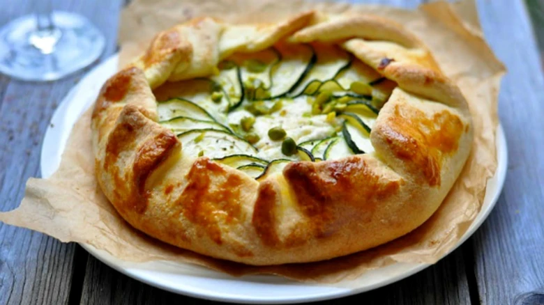 Zlatá koláčová pizza s rikota, cuketou na bílém talíři.