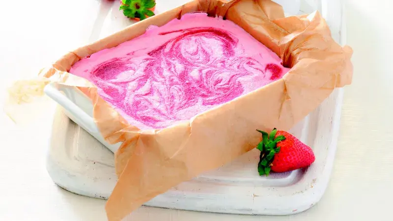 Růžová zmrzina s mascarpone v papírovém podkladu vedle jahody.