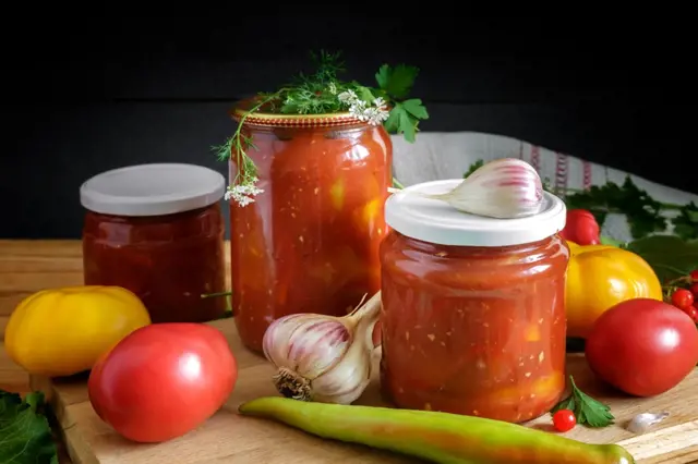 Sklenice domácího leča s čerstvými rajčaty, paprikou a cibulkou na dřevěném prknu.