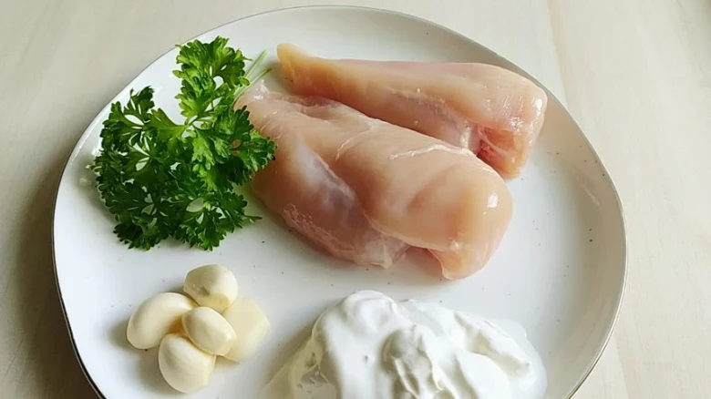 Surové kuřecí prsa s jogurtem, česnekem a petrželkou na talíři.