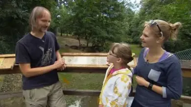 Tři lidé stojí u rybníka v přírodě.