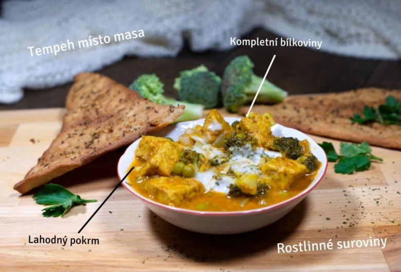 Mísa s tempeh kariem, brokolicí a chlebem na dřevěném podkladu.