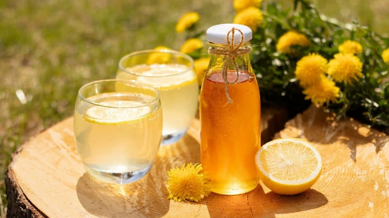 Sklenička s pampeliškovým sirupem, citrony a květy na dřevě.