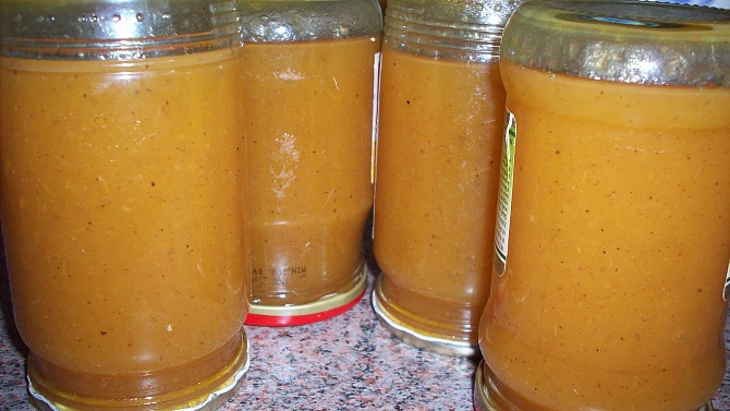Sklenice dýňové marmelády s jablky a skořicí na kuchyňské desce.