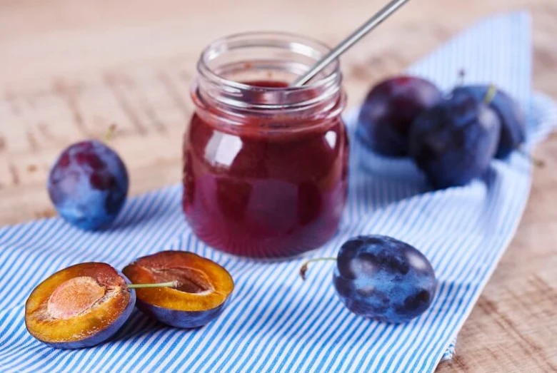 Sklenice domácí švestkové marmelády s čerstvými švestkami.