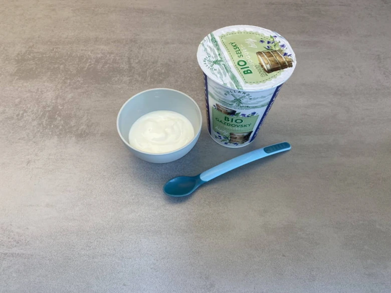 Řecký jogurt v nádobě s lžičkou pro miminko na stole.