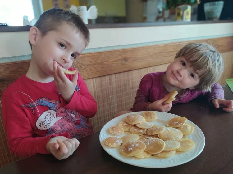 Děti jedí lívance na talíři v kuchyňském prostředí.