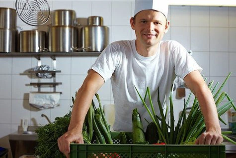 Šéfkuchař drží krabici čerstvé zeleniny v kuchyni.