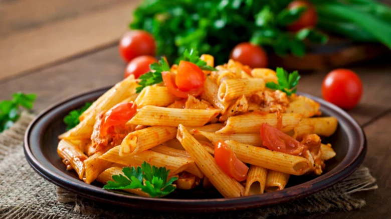 Penne s kuřecím masem v rajčatové omáčce na talíři.