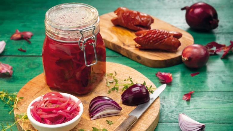 Sklenice marinované červené cibule s nakrájenou cibulí na dřevěném prkénku.