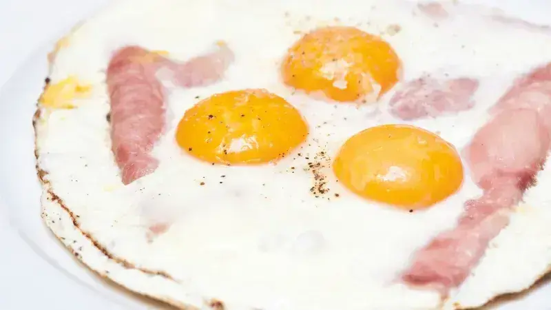 Smažená vejce se slaninou na bílém talíři.