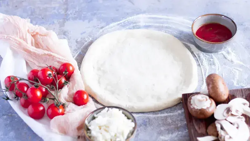 Těsto na pizzu s ingrediencemi jako rajčata a houbami.