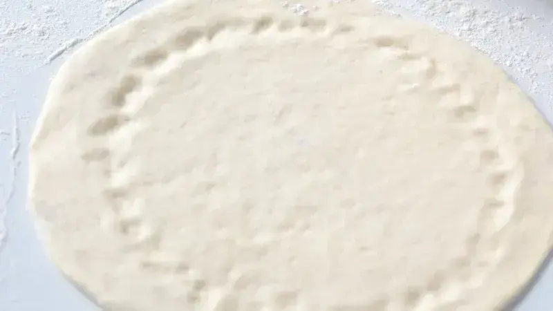 Kynuté těsto na pizzu s vypracovaným okrajem před pečením.