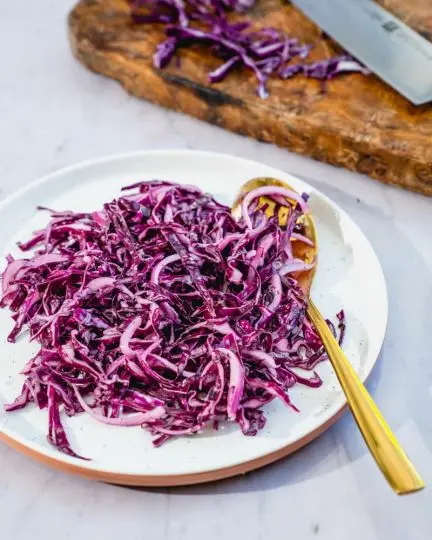 Příprava salátu coleslaw z červeného zelí na talíři.