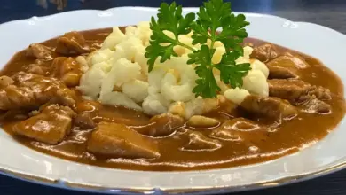 Český guláš s knedlíky v tmavé jíšce na bílém talíři.