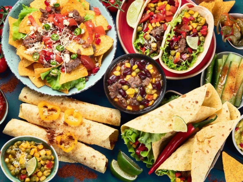 Různá mexická jídla jako taquitos, nachos a tacos s čerstvou zeleninou.