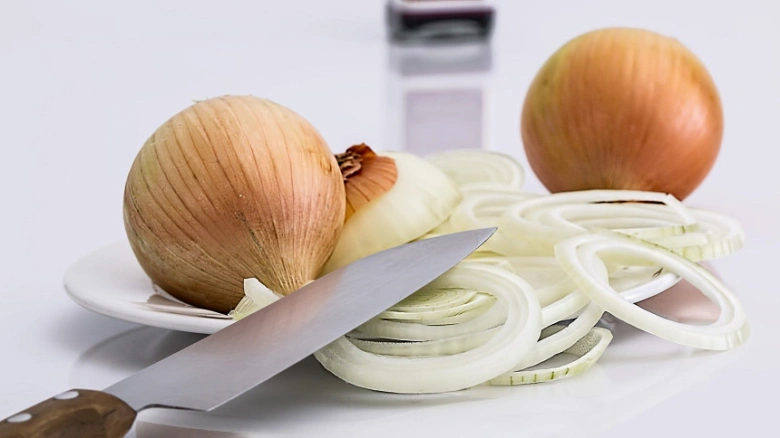 Žluté cibule nakrájené na kroužky s nožem na bílém talíři.