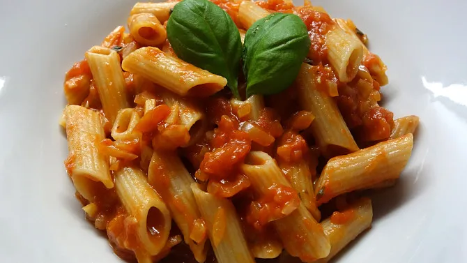 Penne s rajčatovou omáčkou bez masa na bílém talíři.
