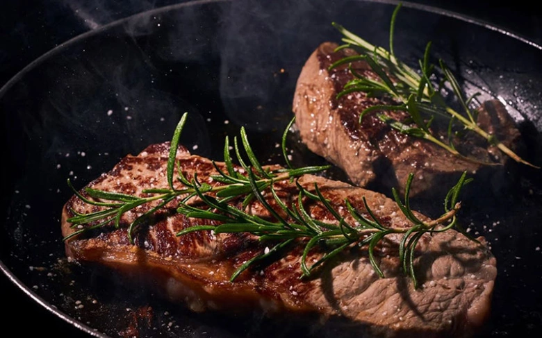 Dva pečené hovězí steak na pánvi s rozmarýnem.