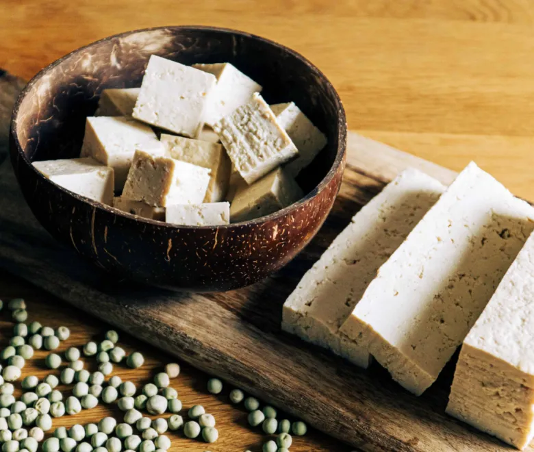 Kostky tofu v kokosové misce s rozsypanými zelenými hráškem.