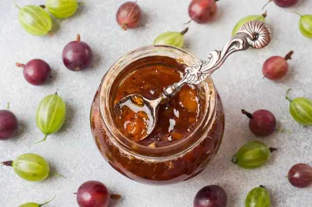 Sklenice angreštové marmelády s lžící a čerstvými plody.