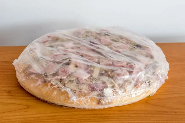Mražená pizza zabalená v plastu na dřevěném povrchu.