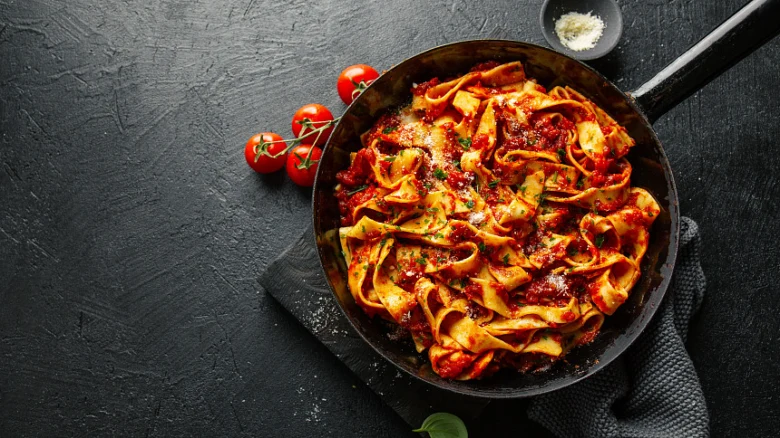 Pasta s rajčatovou omáčkou v pánvi na tmavém povrchu.
