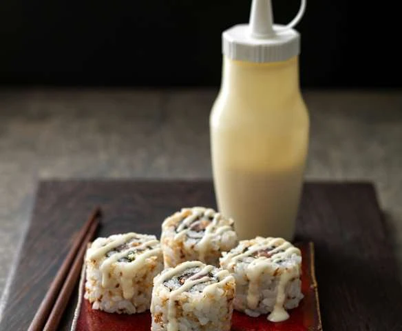 Čtyři kusy sushí polité domácí japonskou majonézou vedle lahvičky.