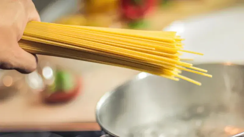 Hand holding spaghetti over pot