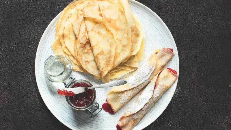 Palačinky s ovocnou marmeládou a moučkou na talíři.