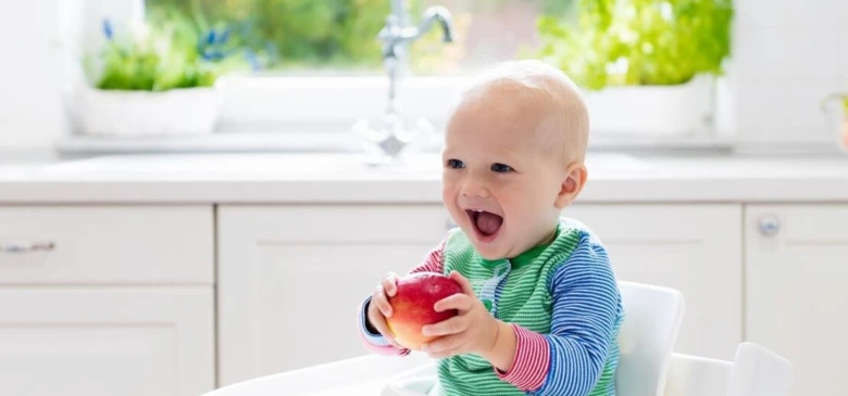 Mimořádně šťastné dítě sedí ve vysoké židli s jablkem.