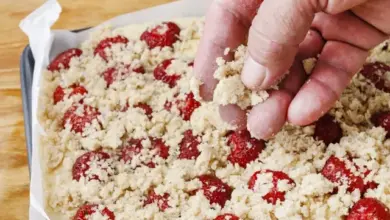 Hand sprinkling crumble topping on berries in baking pan