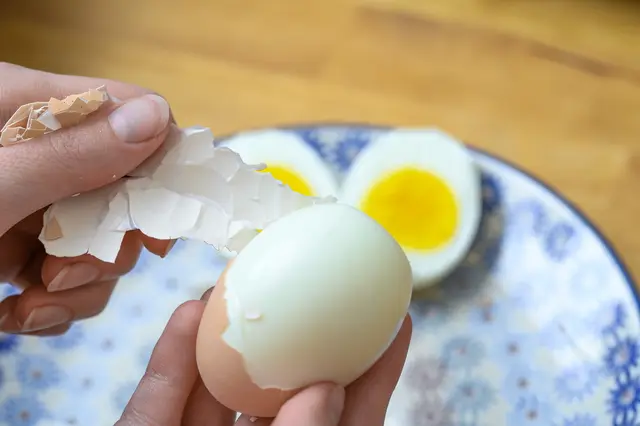 Ruční odstraňování skořápky z uvařeného vejce s viditelným žloutkem.