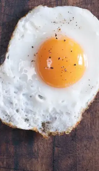 Přesně uvařené volské oko s pepřem na dřevěném povrchu.