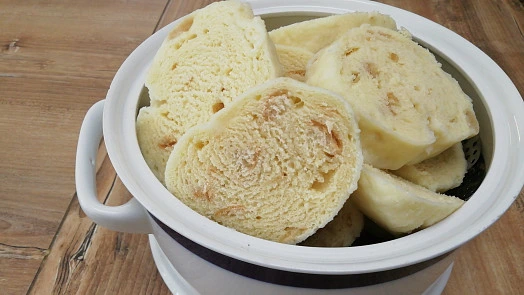 Uvařené knedlíky nakrájené v bílé misce na dřevě.