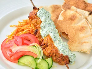 Hotový domácí kebab s omáčkou, chlebem a zeleninou na talíři.