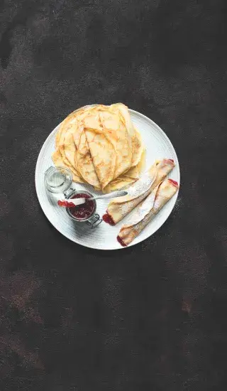 Bílý talíř s palačinkami, klobásou v těstě a džemem.