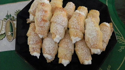 Košíčky s mascarpone posypané cukrem na černém talíři.