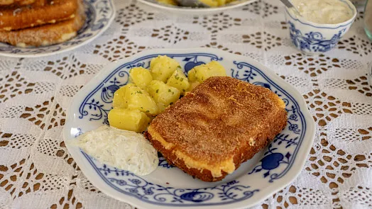 Připravený obalovaný sýr se bramborami a omáčkou na talíři.