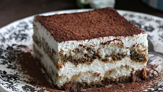 Kousek tiramisu s vrstvami krému z masepánu na talíři.