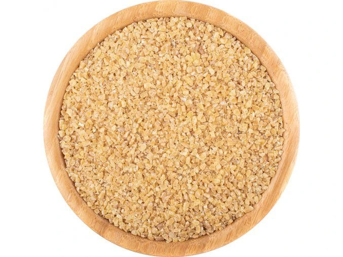 Nevysvařený bulgur v dřevěné mísce na bílém pozadí.