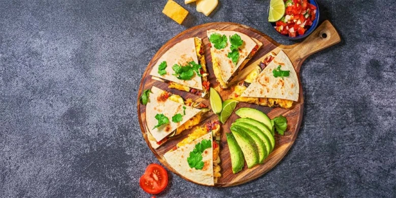 Složené quesadilly s avokádem a rajčatovou omáčkou na dřevěném podnosu.