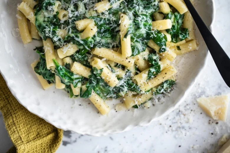 Pasta s baby špenátem v krémové omáčce na bílém talíři.