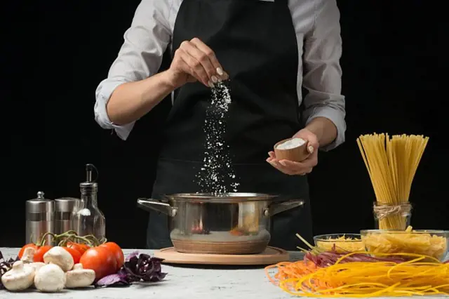 Člověk solí vodu pro vaření těstovin s čerstvými ingrediencemi.