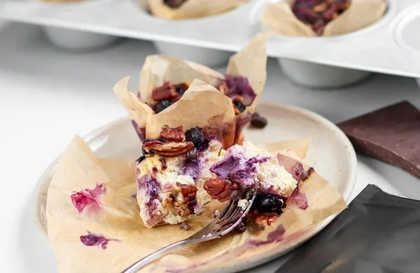 Část tvarohového muffinu s borůvkami, ořechy a čokoládou na talíři.