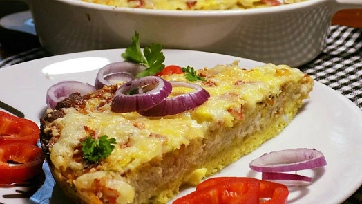 Kousek pečeného chleba ve vajíčku s cibulí a bylinkami na talíři.