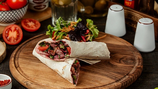 Domácí kebab v tortille s salátem na dřevěném talíři.