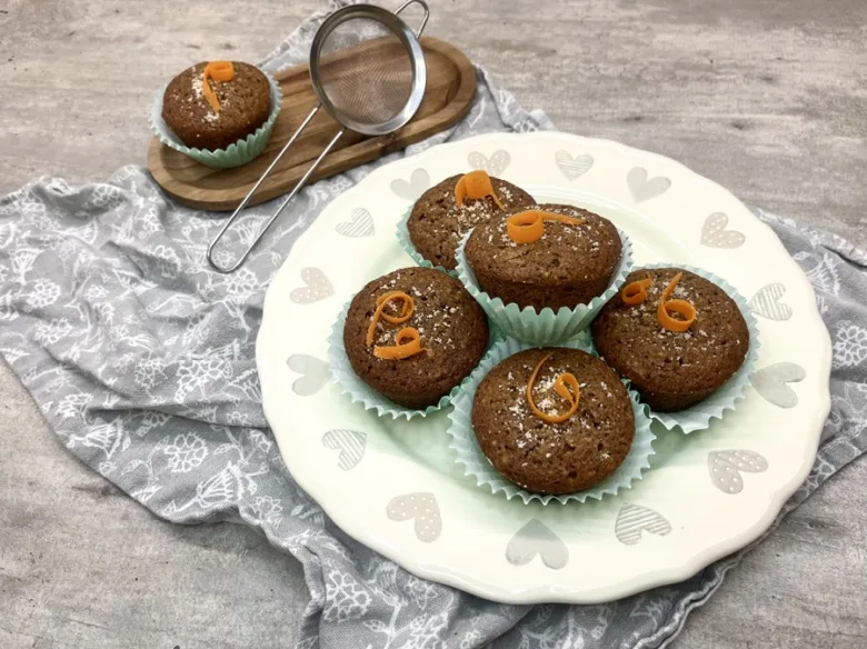 Pět bezlepkových muffinů s kousky pomeranče na talíři.