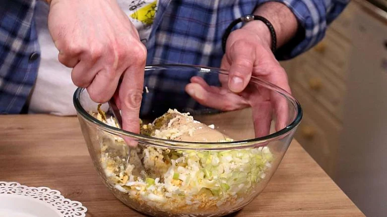 Ruční míchání ingrediencí pro staročeskou škvarkovou pomazánku v skleněné misce.