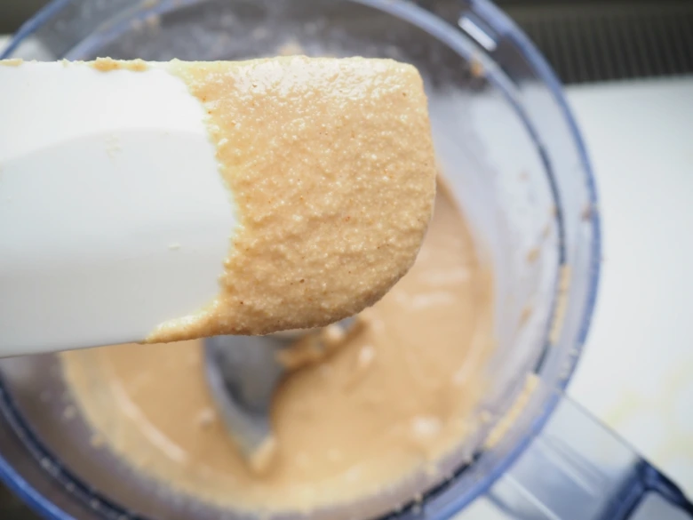 Bílá lžička s hladkou omáčkou z tahini nad mixérem.